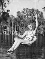Portrait of a young woman sitting on a swing at the lakeside and smiling
