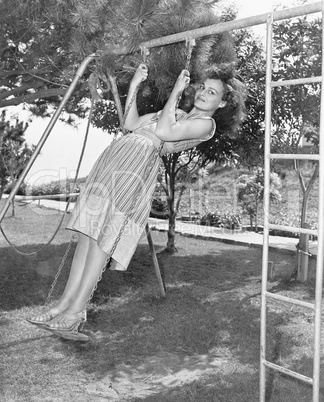Profile of a young woman swinging on a swing in a garden