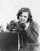 Young woman holding a glass of milk and talking on a rotary phone