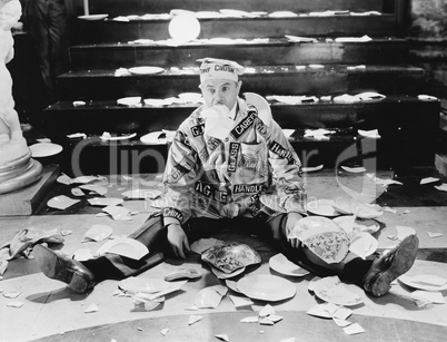 Man sitting in front of a staircase with broken plates around him