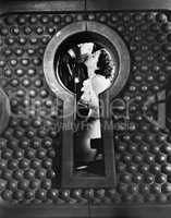 Image of a couple kissing viewed through a keyhole