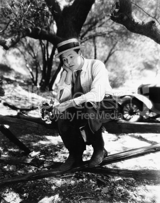 Man sitting on a fence with flowers in his hands and looking sad