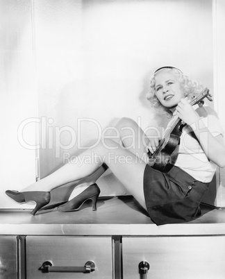Profile of a young woman sitting on a counter playing a guitar