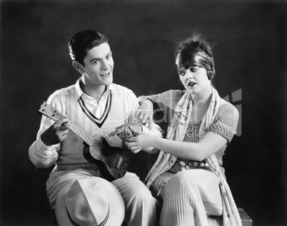 Young man holding a guitar with a young woman teaching him how to play
