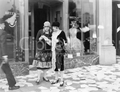 Two women in the street reading papers being thrown down from an office