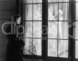 Woman standing outside of a window watching a woman trimming a Christmas tree
