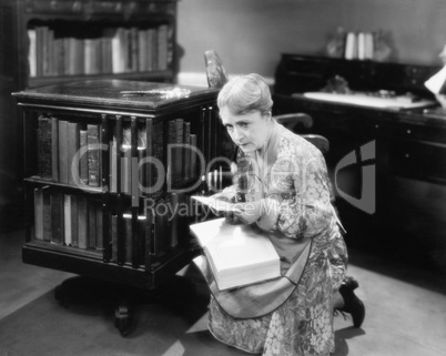 Woman kneeling with a book in her library finding a letter