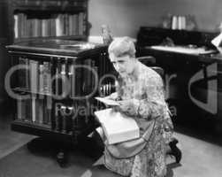 Woman kneeling with a book in her library finding a letter