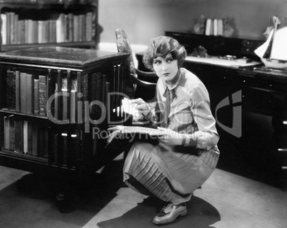 Woman kneeling with a book in her library finding a letter