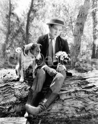 Young man sitting in the woods with his dog looking forlorn