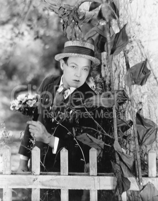 Young man hiding behind a tree with a bouquet of flowers in his hands