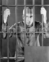 Prisoner behind bars looking angry and sad