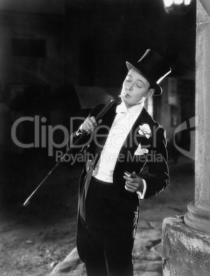 Young man in formal clothing lighting his cigarette with his walking stick