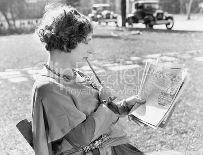 Woman with a pencil in her mouth reading the newspaper