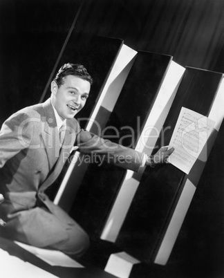 Man sitting with oversized books holding sheet music in his hands