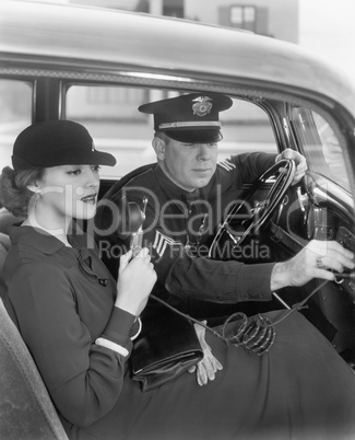 Woman sitting next to a policeman in his car holding a microphone in her hand