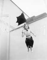 Young woman is blown away, jumping from a roof with an umbrella