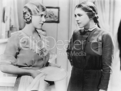 Two young woman talking with each other while doing the dishes