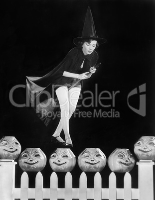 Young witch hovers on her broom, eyeing which pumpkin to choose