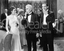 Three people standing together at a formal party yawning and being bored