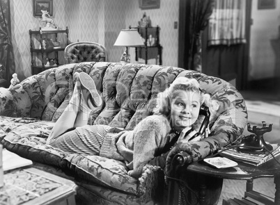 Young woman lying on a sofa in a living room and talking at the phone