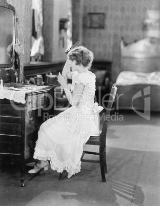 Young woman sitting in front of her vanity table and grooming her hair