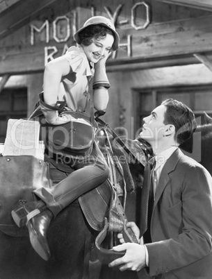 Woman sitting on a horse talking and flirting with a young man