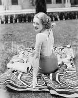 Young woman sitting in a sun suit on a lawn scratching her back