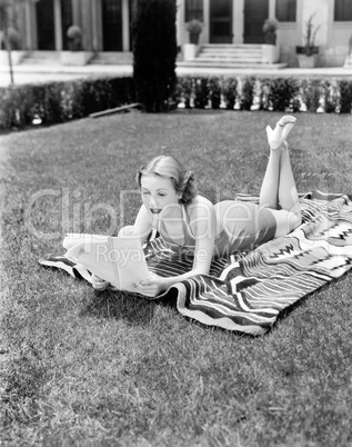 Young woman lying on a towel in her yard sunbathing and reading