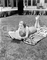 Young woman lying on a towel in her yard sunbathing and reading