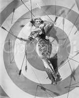 A target of desire, a young woman lying on the bulls eye with arrows around her