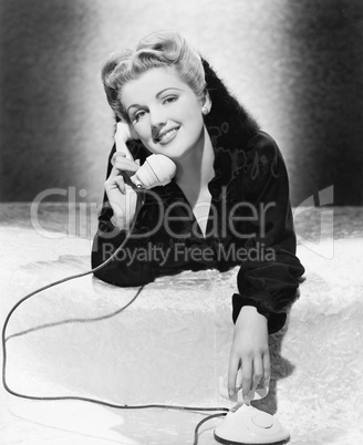 Young woman lying on her stomach and talking on the telephone