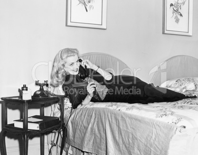 Young woman lying on her bed in the bedroom and talking on the telephone