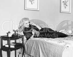 Young woman lying on her bed in the bedroom and talking on the telephone
