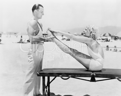 Trainer and young woman doing exercises at the beach