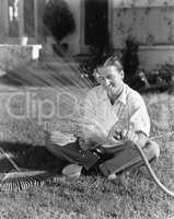 Man watering the grass and reading