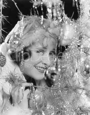 Young woman looking through the branches of a Christmas tree with ornaments