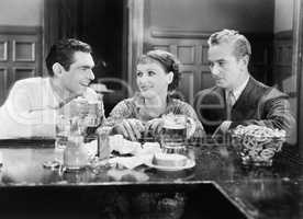 Two men and a woman sitting at a bar drinking beers