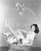 Young woman, looking like a present, sitting in gift basket with bunnies