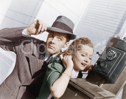 Man and woman listening on an outside telephone
