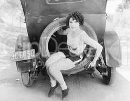 Young woman sitting in the extra wheel of a car