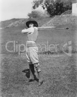 Young woman swinging a golf club on a golf course