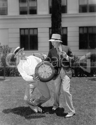 Two men wrestling with an oversized pocket watch