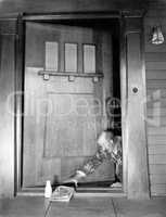 Man crawling at the front door to reach his newspaper and milk