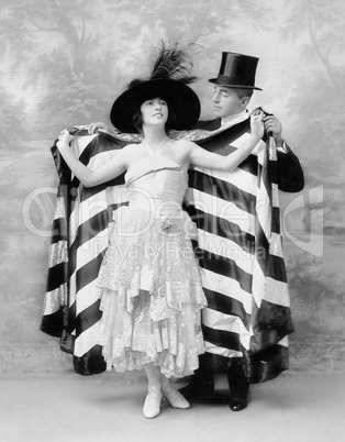Man in a top hat helping a woman into a cape
