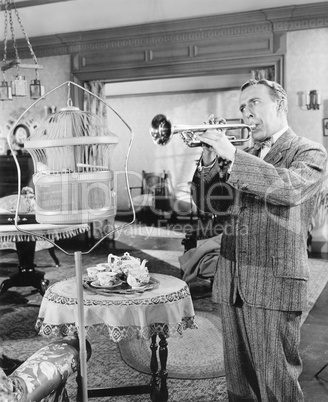 Man standing in his living room playing the trumpet to a bird
