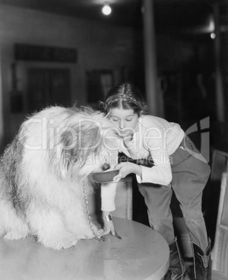 Young woman offering her bearded collie a drink of water