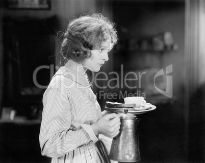 Young woman carrying a pot of coffee and a plate with bread
