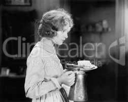 Young woman carrying a pot of coffee and a plate with bread