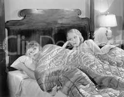 Two women together in bed under a blanket